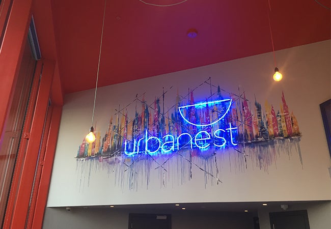 A funky neon sign that says "Urbanest" in lowercase letters hang above an entryway. 