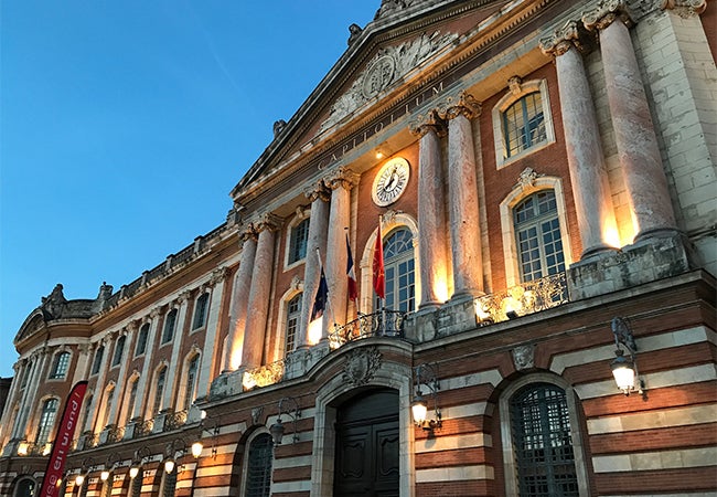 Lights illuminate stone columns along the exterior of the Capitole de Toulouse during evening in France. 