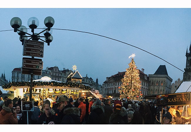 Shoppers peruse wares at a Christmas market adorned with holiday lights in Prague during the early evening. 