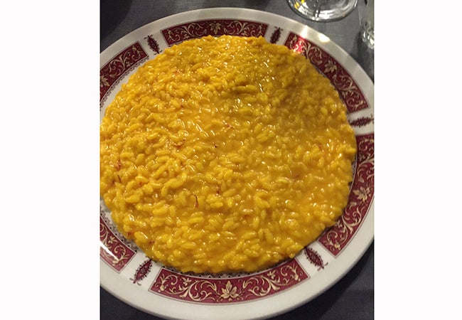 A close-up shows a plate of bright orange risotto alla milanese. 