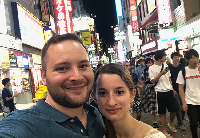 Ryan and his girlfriend take a selfie on a busy street at night, surrounded by pedestrians and lighted signs.