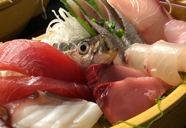 A close-up photo shows raw fish of various colors and types piled on top of one another. 