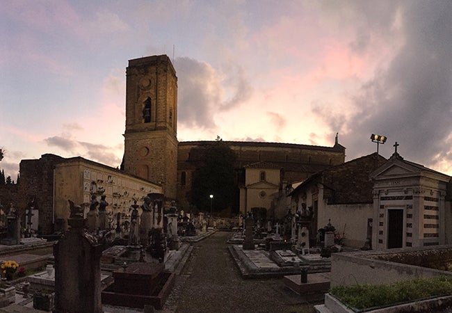The sun sets behind an old stone church in Florence with a small cemetery in front. 