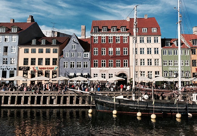 Pedestrians make their way through a row of white tents along a waterway in Copenhagen.