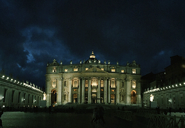 Dark clouds hover above a tall stone building framed by large columns at night. 