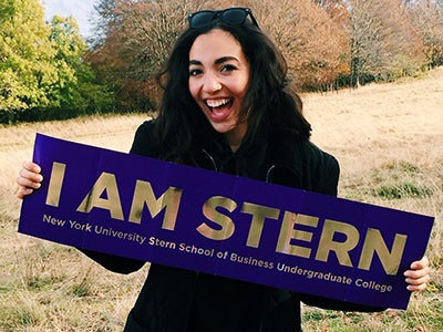Undergraduate business student Alexandra Grieco holds a purple banner that says "I am Stern" in gold letters while studying abroad. 