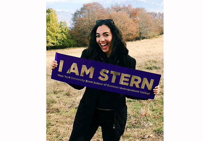 Undergraduate business student Alexandra Grieco holds a purple banner that says "I am Stern" in gold letters while studying abroad. 