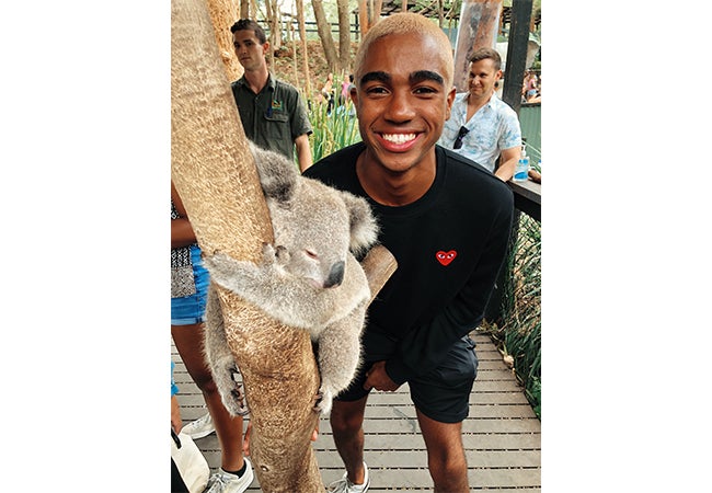 Undergraduate student Dimitri Pun smiles next to a fluffy koala as it hugs a tree at a wildlife park in Sydney, Australia. 