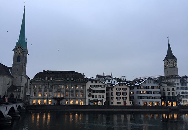 Evening sets on buildings in Zurich, framed by a tall green steeple. 