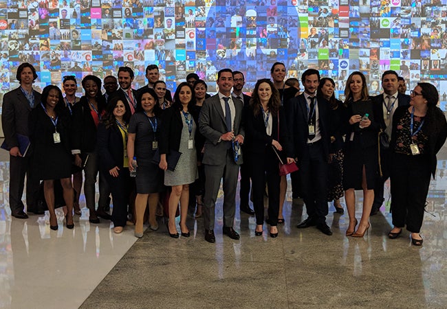 A group of Executive MBA students in India are pictured in front of a large digital display screen.