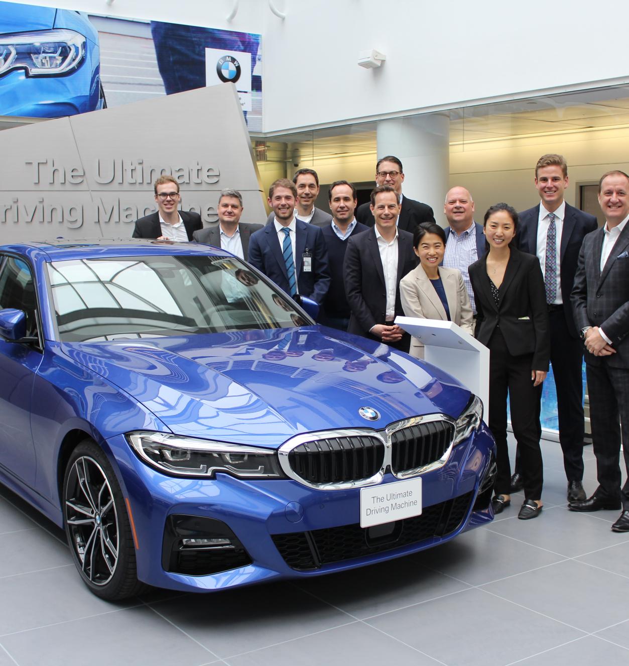 A smiling group of people standing beside a blue car