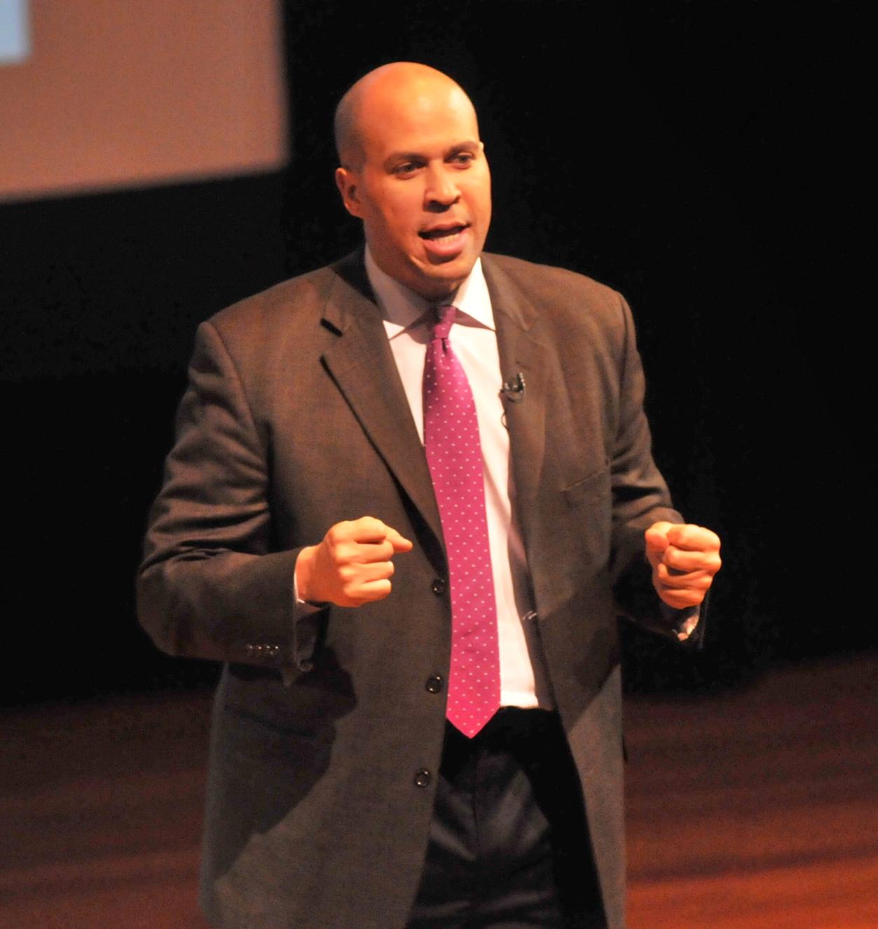 Senator Cory Booker speaking at Business & Its Publics Plenary Man in a suit speaking on a stage
