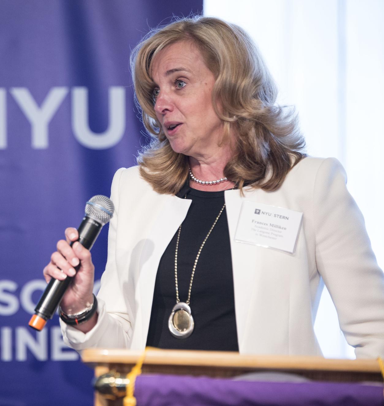 Professor Frances Milliken speaking at a podium in front of an NYU Stern banner