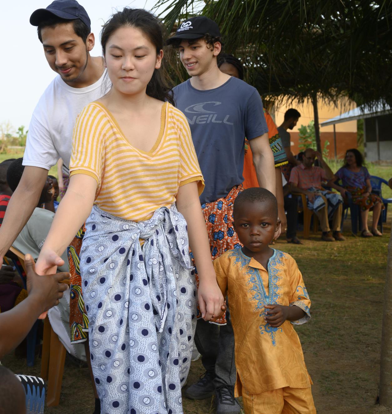 Students walking down a line and shaking hands. The girl in the front is holding hands with a child