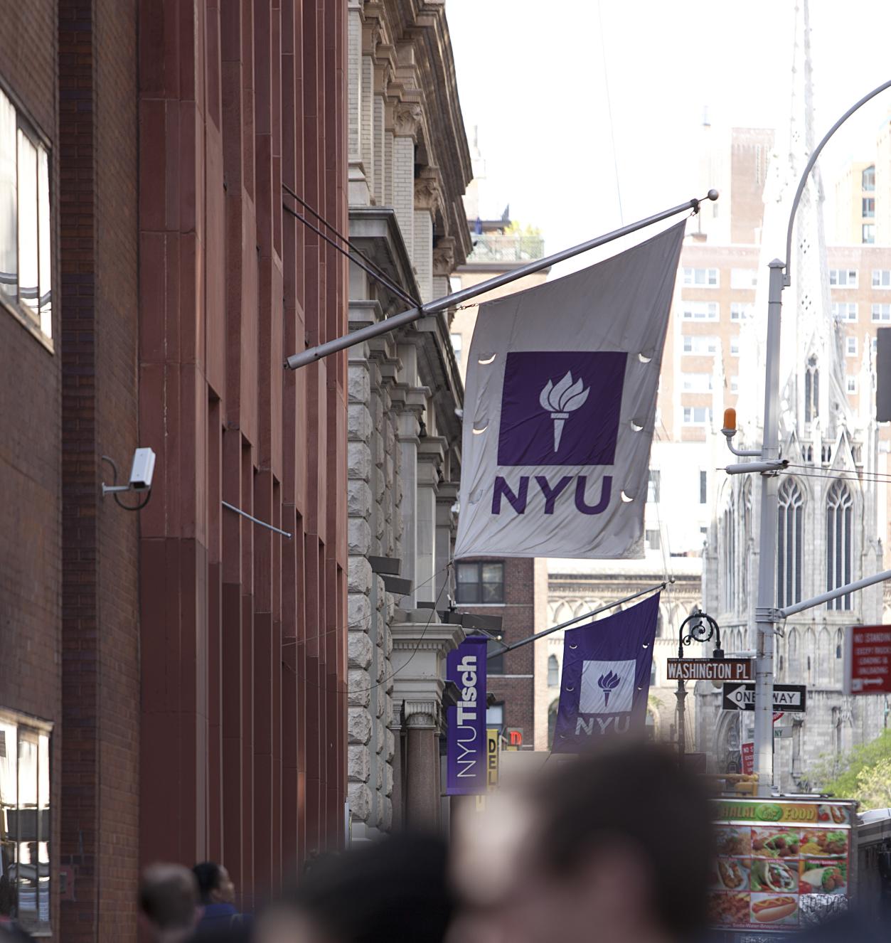 View of sidewalk with blurry crowds below an NYU Banner