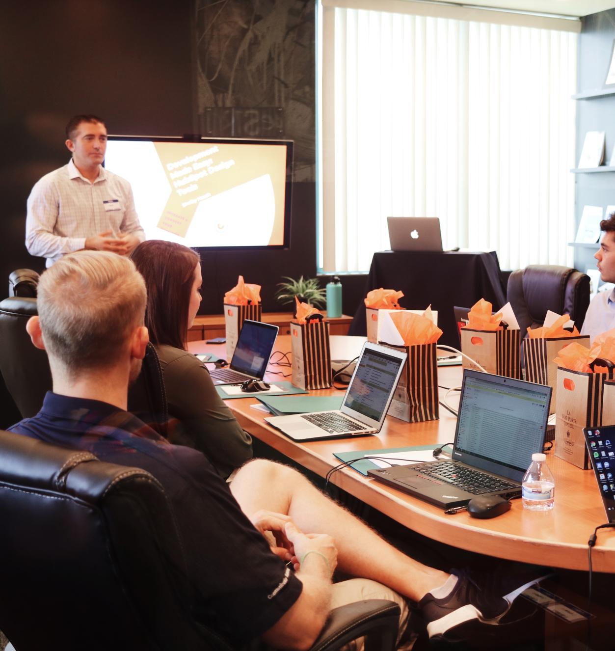 A group of people sitting around a conference table listening to a man presenting at the head of the table