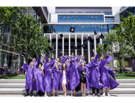 Students in violet graduation attire throwing their caps in the air. 