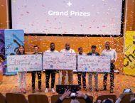 Winning teams stand on stage with prize checks as confetti falls