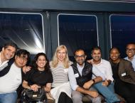 A group of 8 people sitting next to each other with the windows of the boat behind them