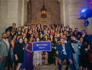 A group of NYU Stern Alumni holding a flag that says "NYU Stern Reunion" celebrate at Reunion 2025.