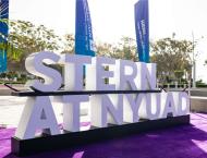 Stern at NYUAD sign with flags in the background