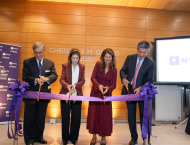 Four people use scissors to cut a large violet ribbon