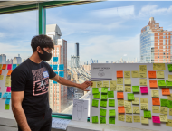 An undergraduate student stands in front of a poster board display that contains colorful Post-It notes