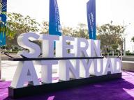 Stern at NYUAD sign with flags in the background
