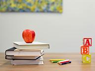 Desk with apple, books, colored pencils and blocks