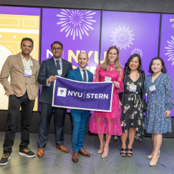 Six alumni pose with an NYU Stern banner at the Reunion 2023 celebration at MoMA.