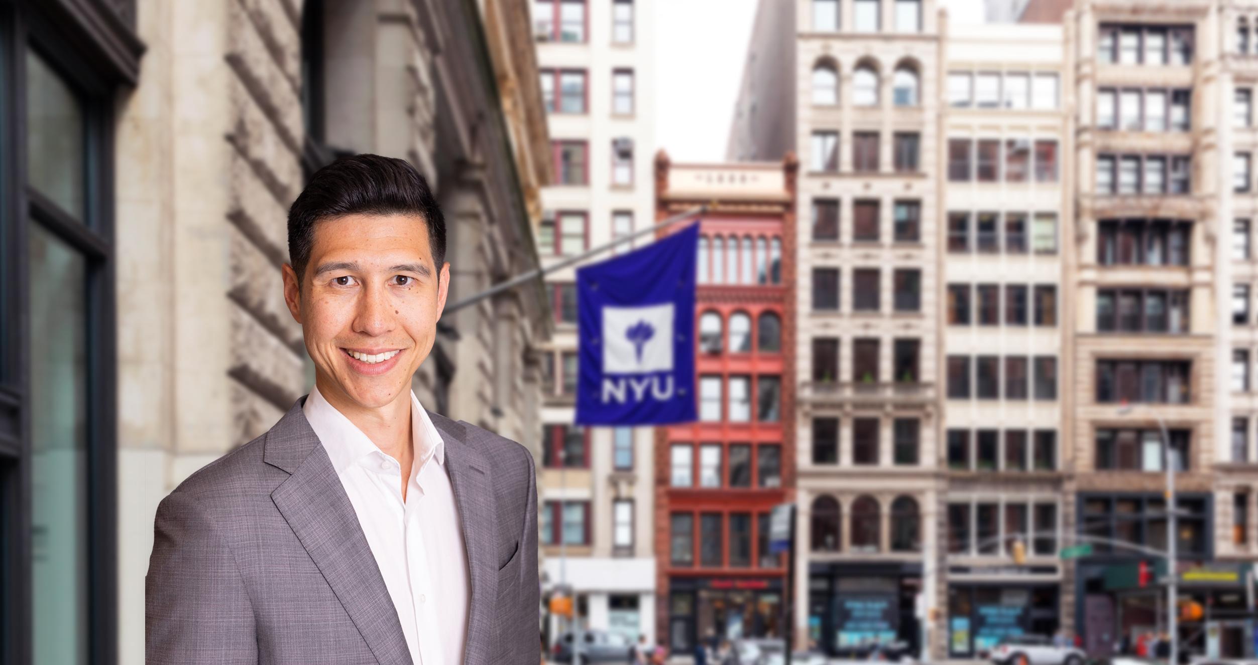 Male student in a grey suit and a blurred background of a street view with a violet New York University flag