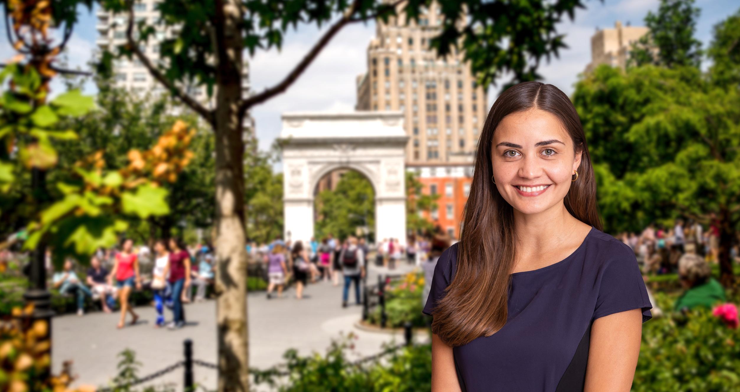 Female student with brown hair and blue dress in front of a blurred background of Washington Square Park