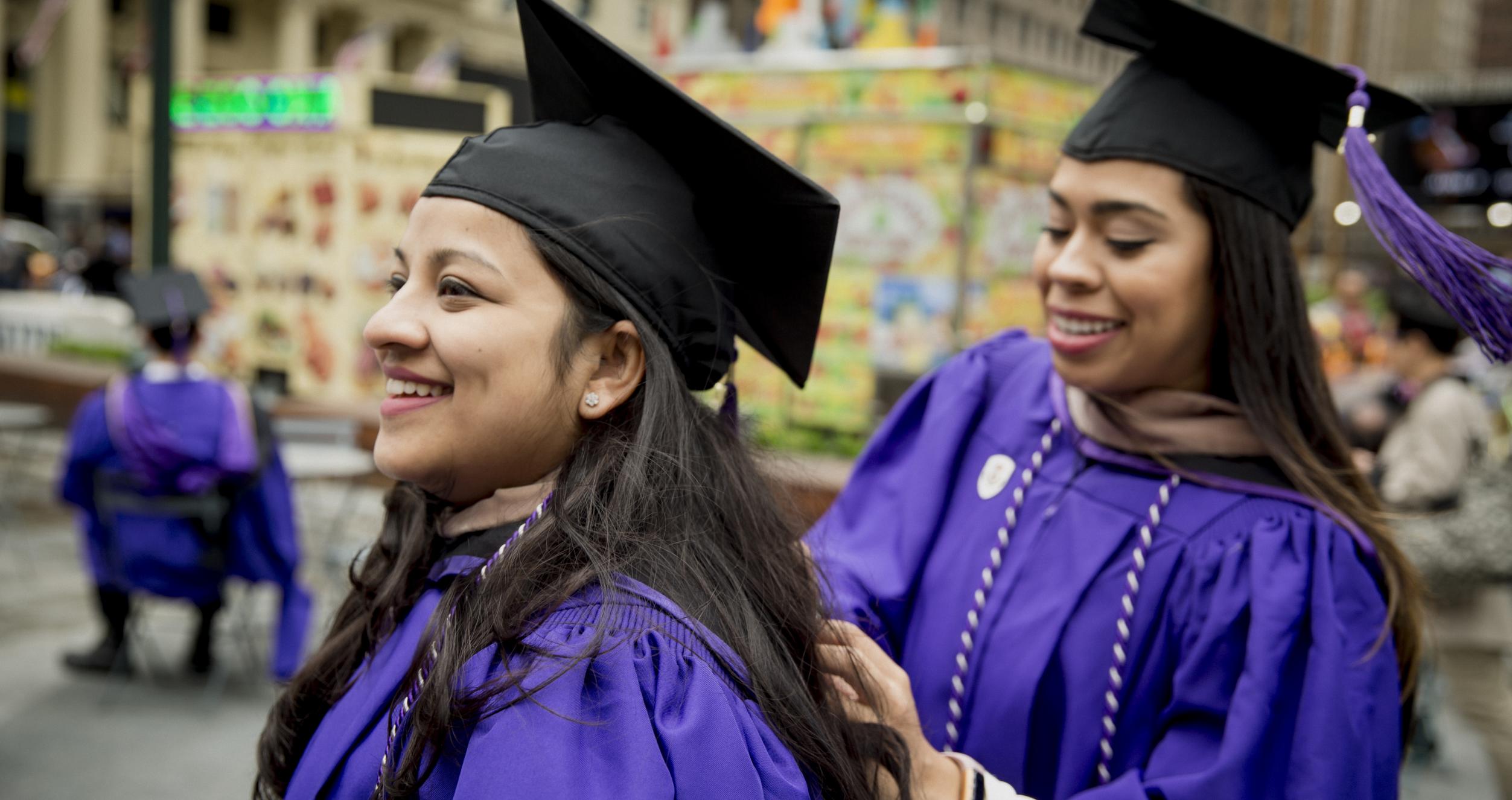 Two students in graduation attire prepare for convocation