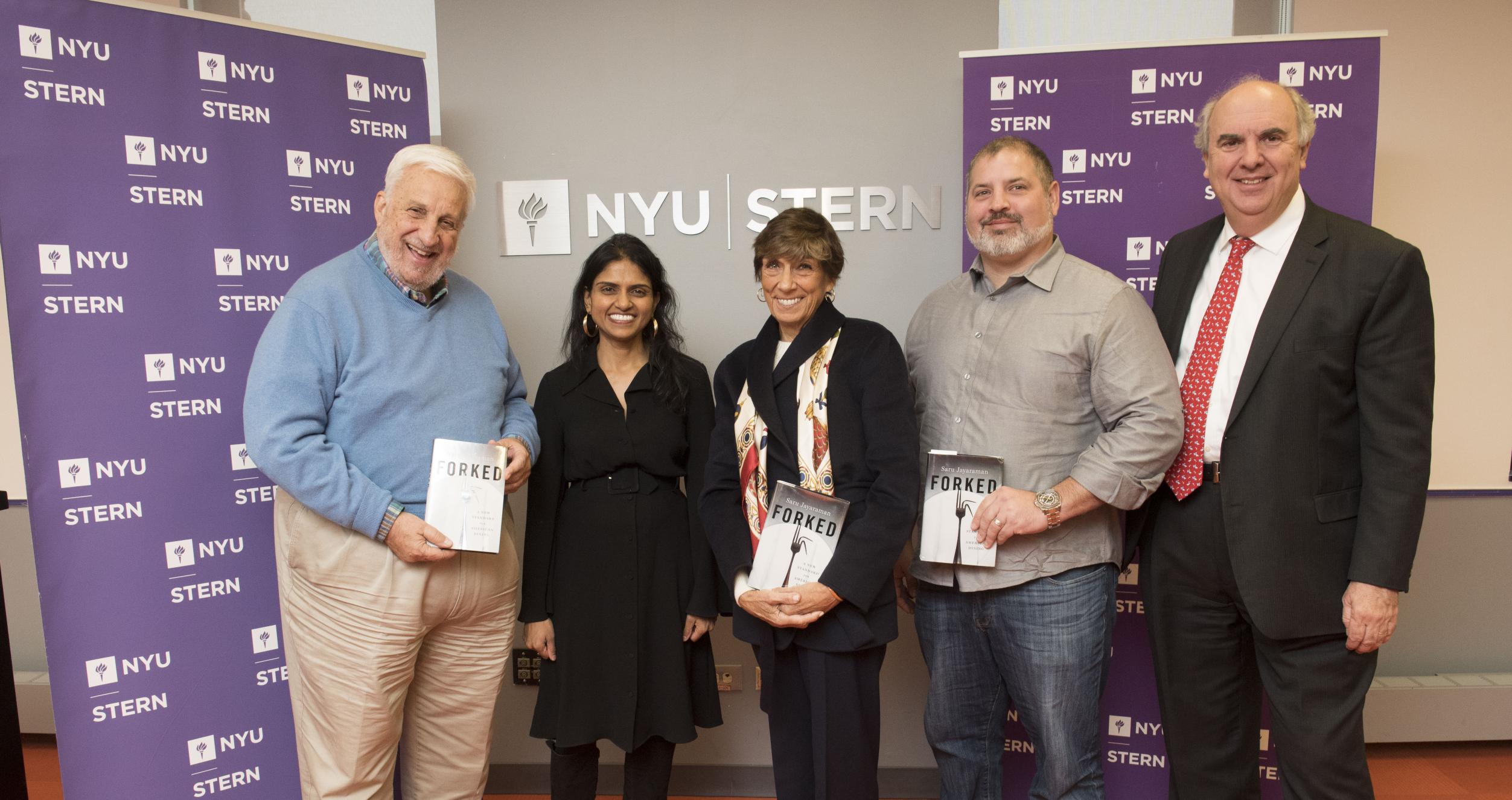 Five people standing in front of a wall with NYU Stern logo, flanked by two purple banners with the NYU Stern logo