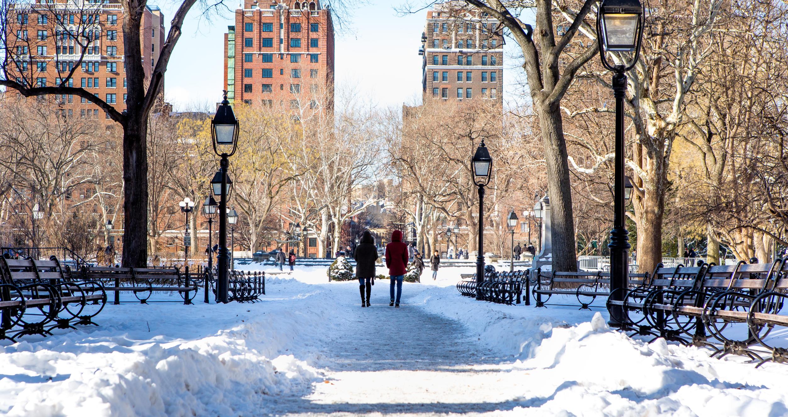 Two students walk down a snowy scene in Washington Square Park