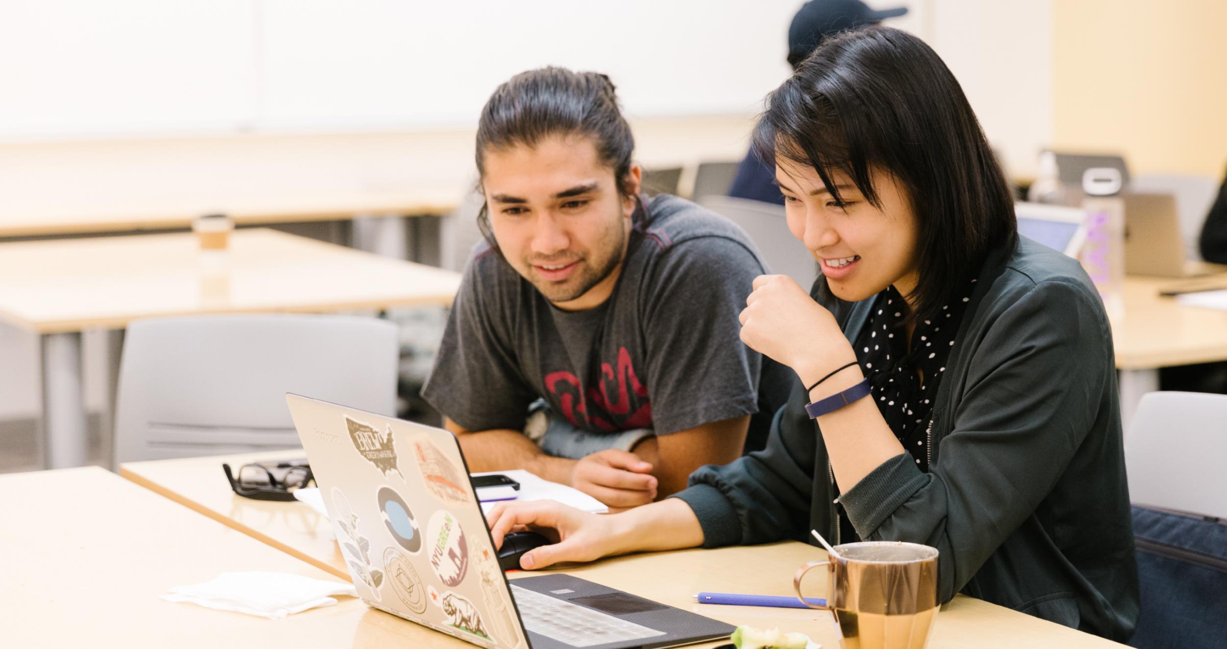 Two NYU Stern students are looking at a computer together in class