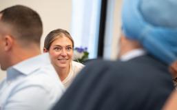 A feminine-presenting person with light skin and hair smiles intently at a partner whose back is to the camera.