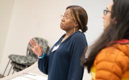 A feminine-presenting person stands with their eyebrows raised and hand raised in defense. 
