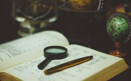 Book with magnifying glass and pen