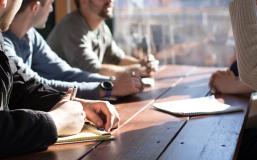 People sitting on chair in front of table while holding pens during daytime