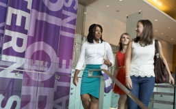 three women in business casual attire looking at each other as they descend a staircase