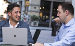 two young men in business clothing sitting at a table with a laptop