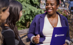 woman holding an nyu stern-labeled folder speaking to other women on a park bench