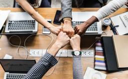 Five people doing fistbumps over a table with laptops