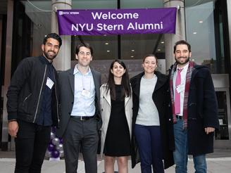 Alumni in front of Welcome NYU Stern Alumni sign in Gould Plaza