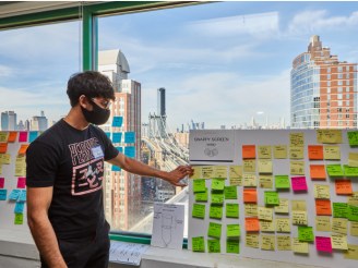 An undergraduate student stands in front of a poster board display that contains colorful Post-It notes