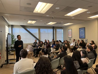 David Ko stands in front of a group of students addressing them in a conference room