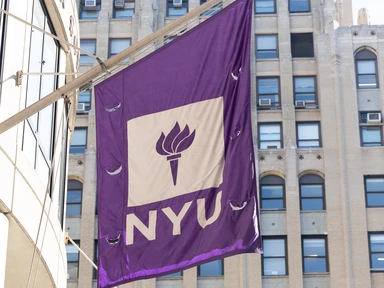 A picture of violet and white NYU flags in front of KMC.