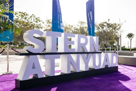 Stern at NYUAD sign with flags in the background