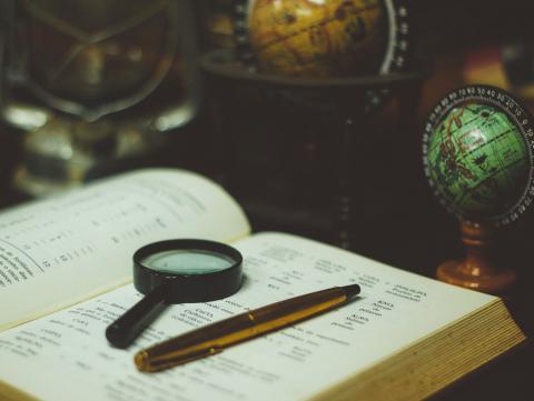 Book with magnifying glass and pen